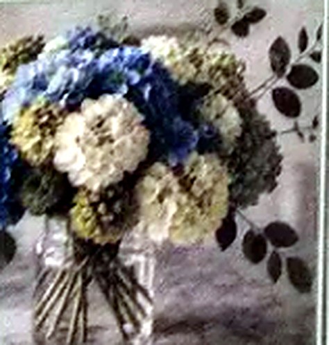 An arrangement of blue and white hydrangeas in a clear glass vase.