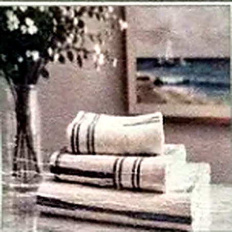 Folded striped linens and towels stacked on a table, with a framed coastal scene behind them.
